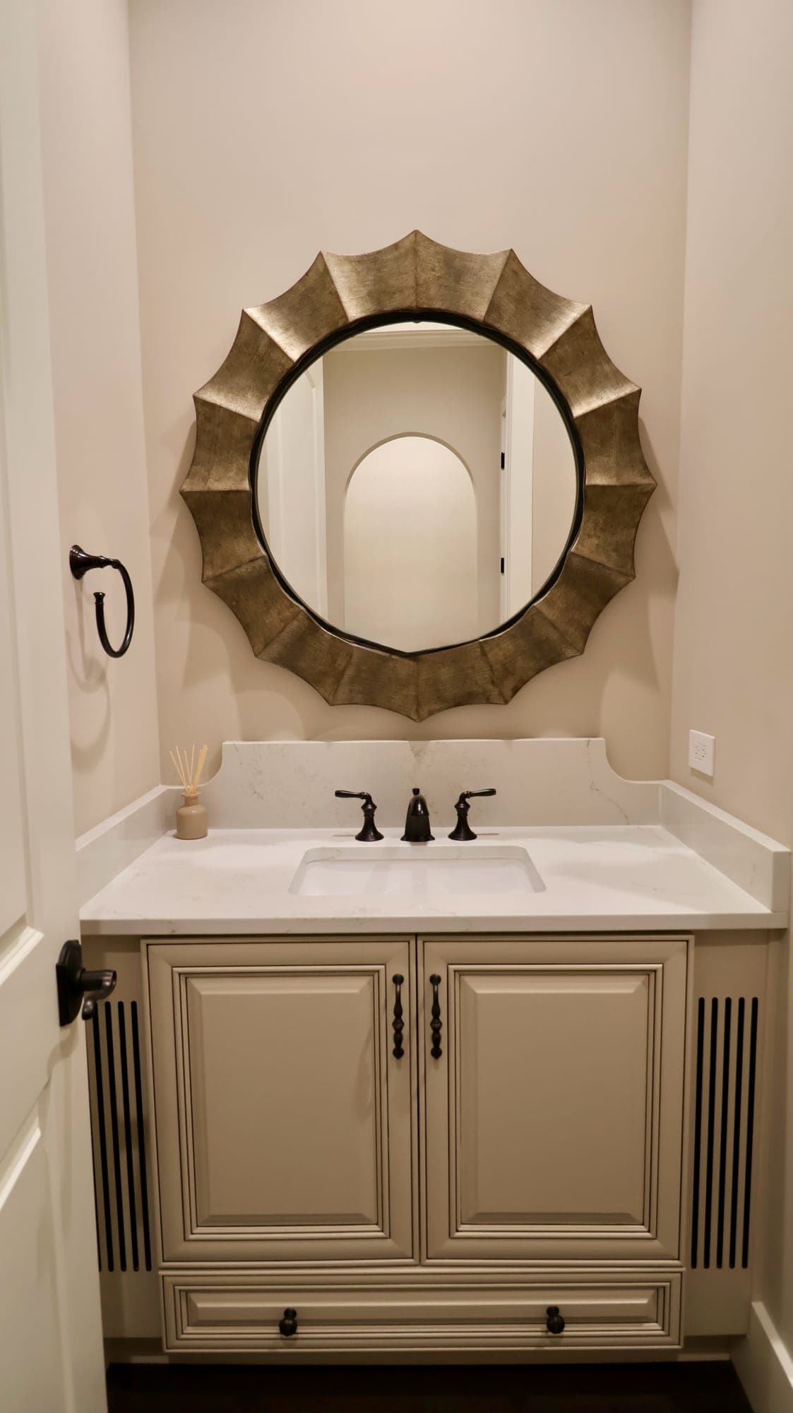 Powder room with a furniture-style vanity, marble top, oil-rubbed bronze faucet, and a sunburst mirror in a custom home in Nocatee, Florida